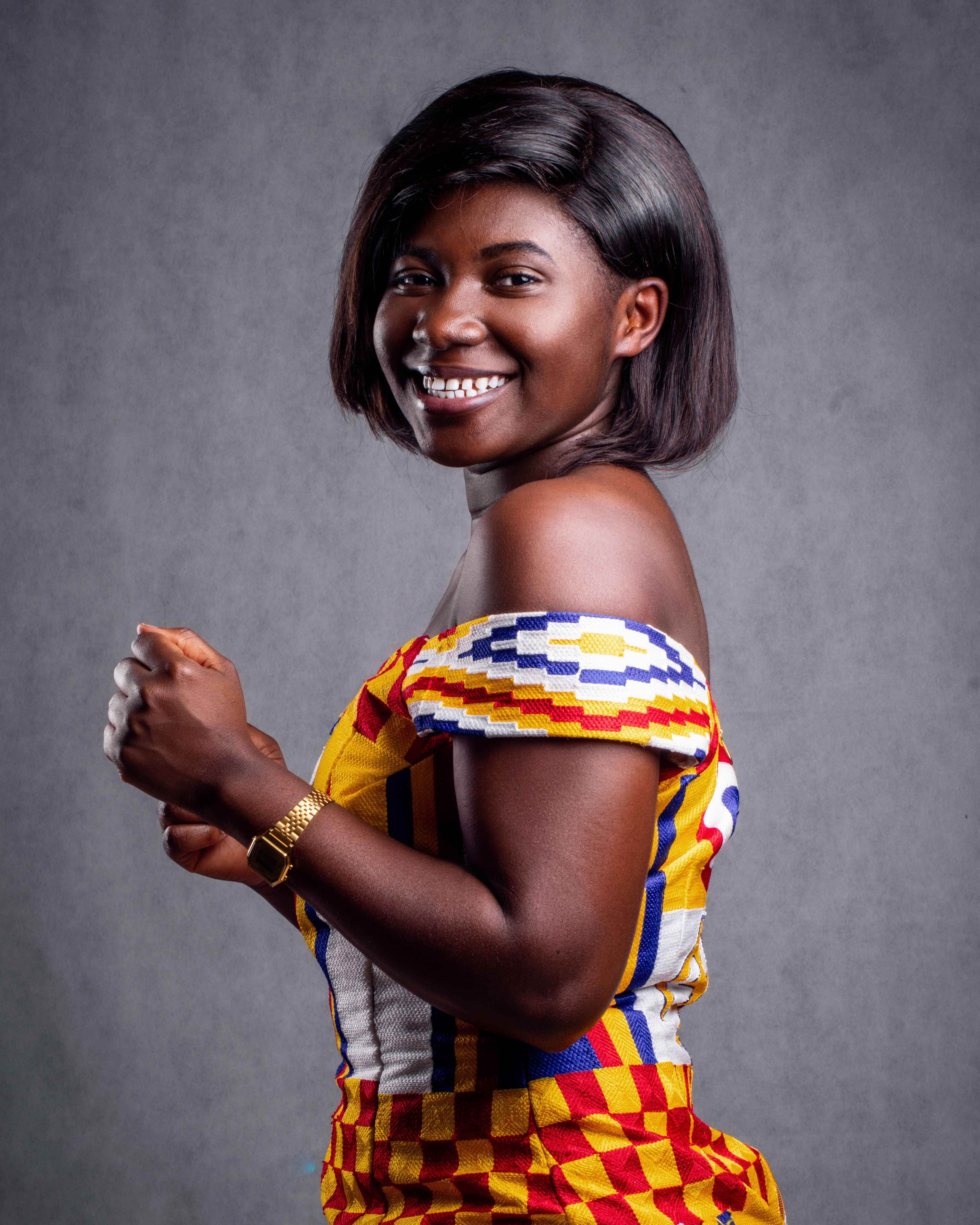 A woman smiling and posing in vibrant clothing in a studio with a gray backdrop.