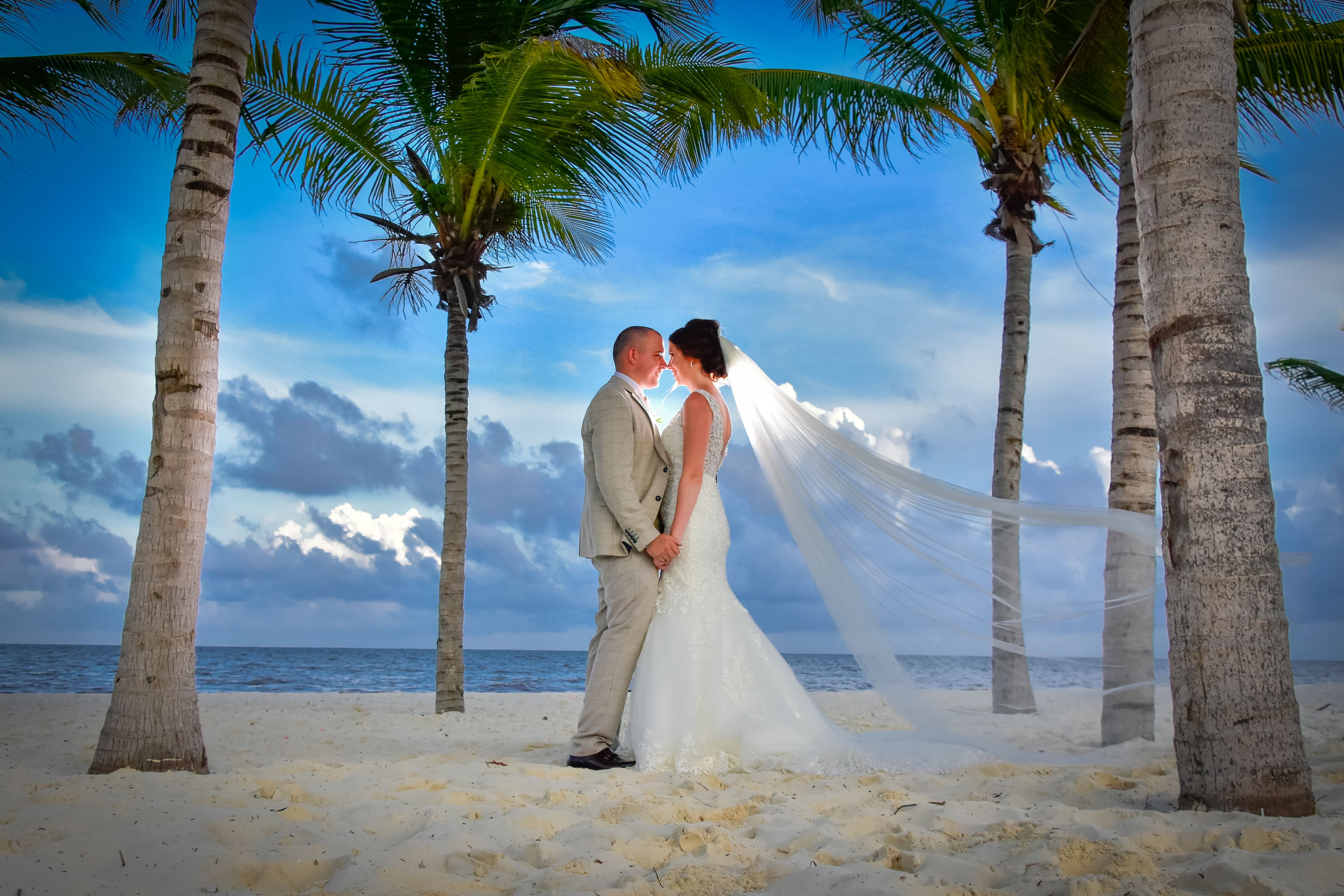 Bride and groom on a tropical beach at sunset with palm trees