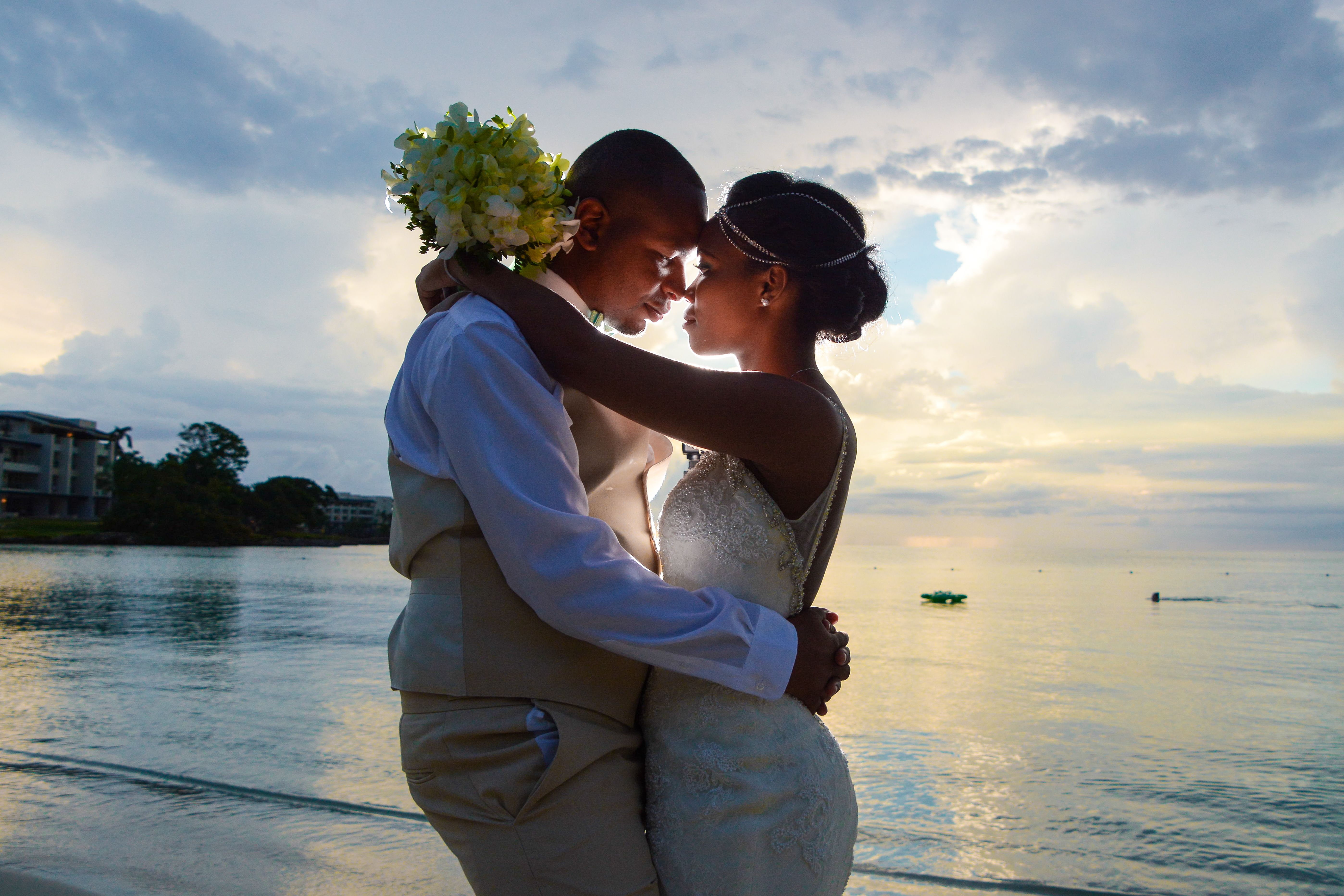 A loving couple embraces on the beach at sunset, celebrating their wedding by the sea.