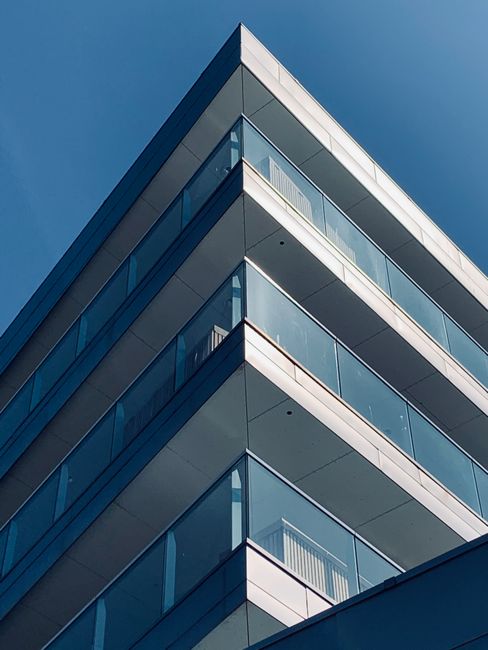 From below of sharp corner of modern geometric building with glass balconies against cloudless blue sky