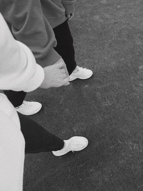 A black and white photo showing a couple walking hand in hand on a pavement dressed in casual wear.