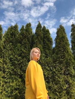 一名年轻女子穿着黄色毛衣，自信地站在绿树蓝天的背景前