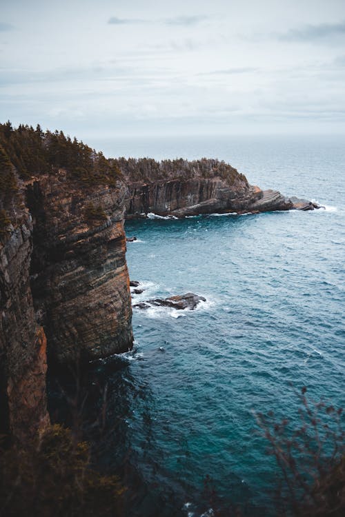 Spectacular scenery of huge rocky cliffs and waving foamy ocean against cloudy sky