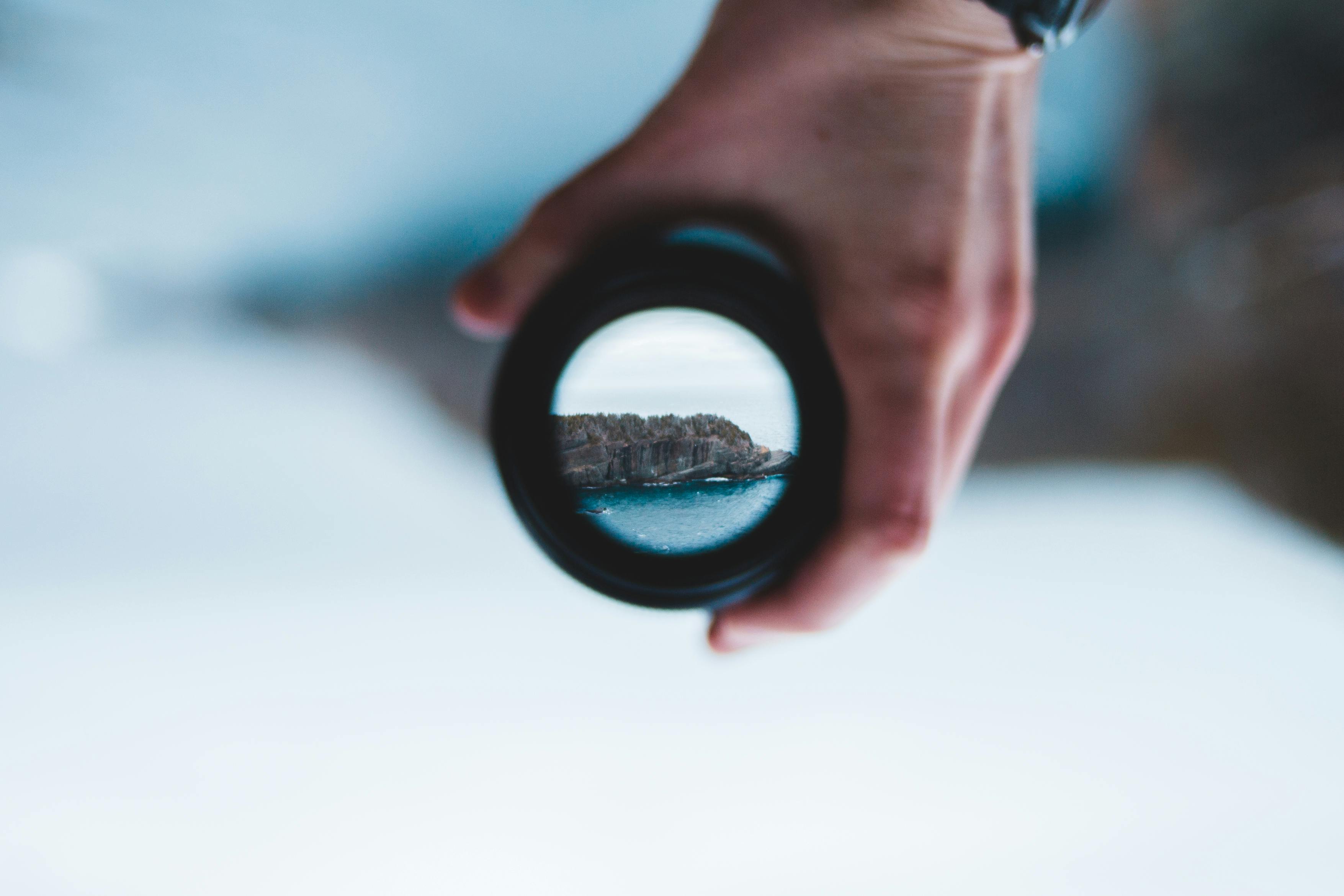 Crop man holding camera lens against sea cliff · Free Stock Photo