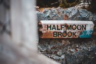 Shabby lumber board with inscription Half Moon Brook placed on rocky stone in nature park