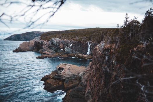 在阴云密布的天空下，被常绿森林包围的悬崖和瀑布直入海洋，景象令人惊叹