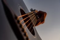 Crop unrecognizable male musician placing fingers on modern acoustic guitar frets while performing in studio