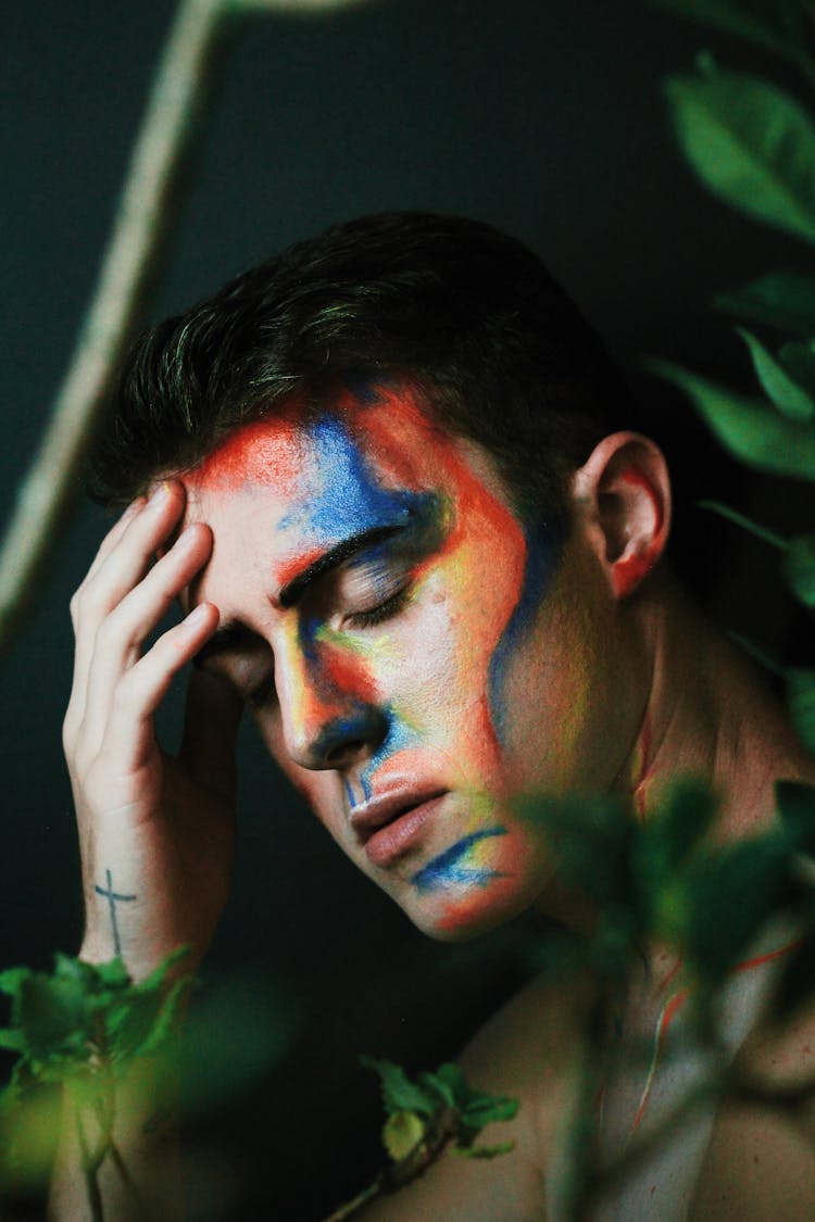 Worried Male Model With Paints On Face And Closed Eyes