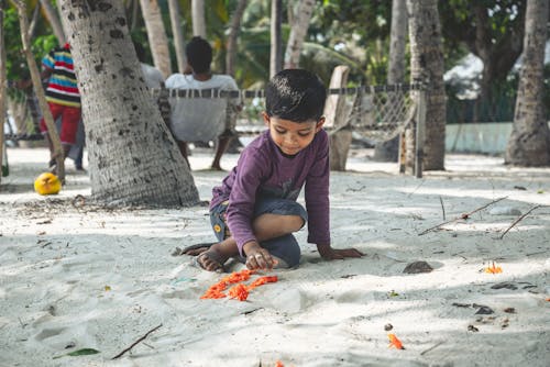 Boy in Purple Long Sleeve Shirt Sitting on Sand