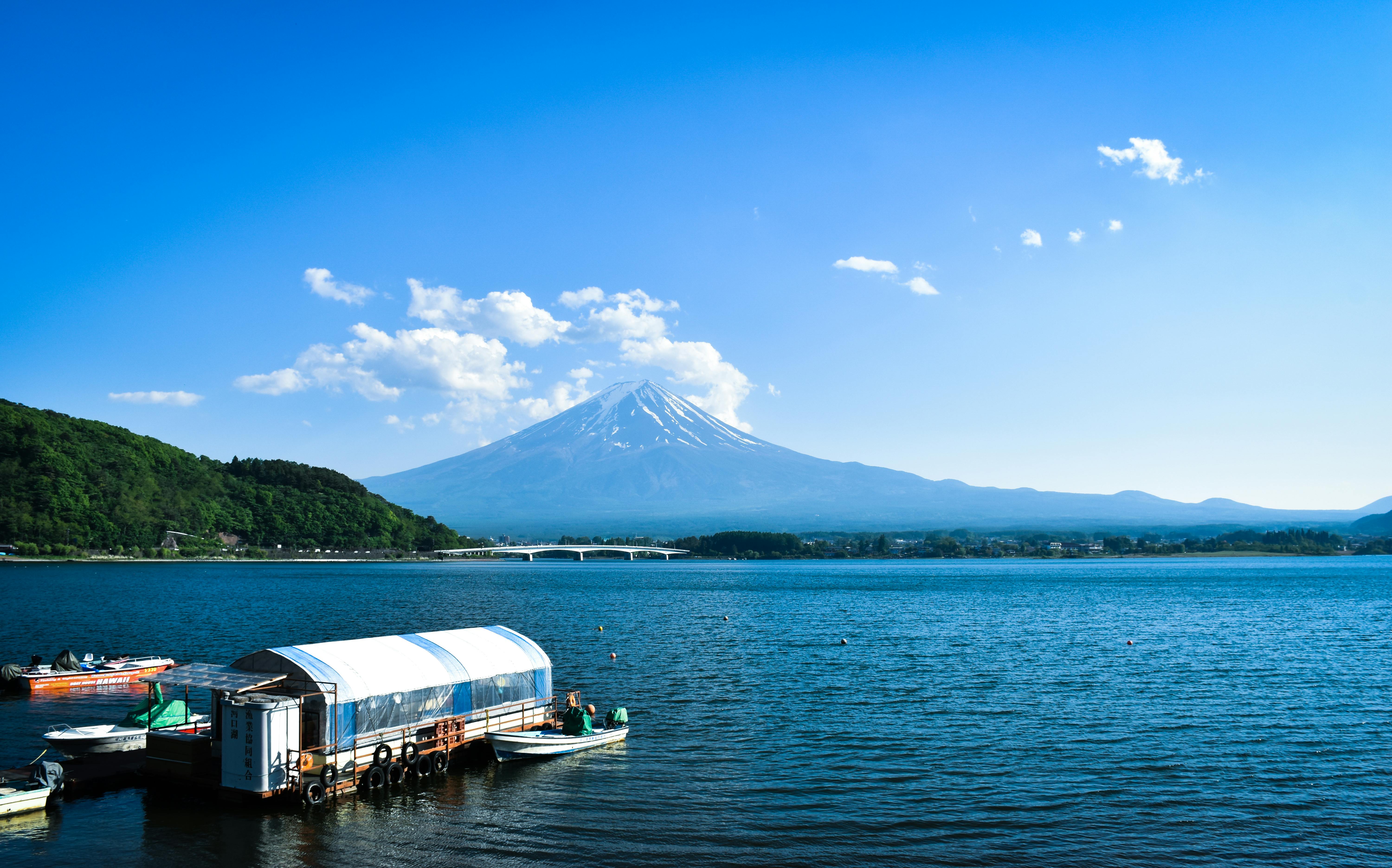 Tranquil scene of Mount Fuji with boats on Lake Kawaguchi, under a clear blue sky.