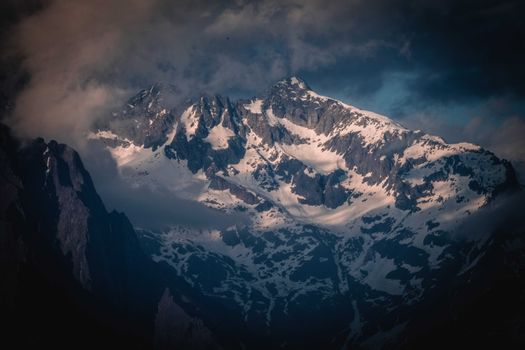 Scenery view of rough ridge with pointed peaks covered with snow under cloudy sky in wintertime in evening