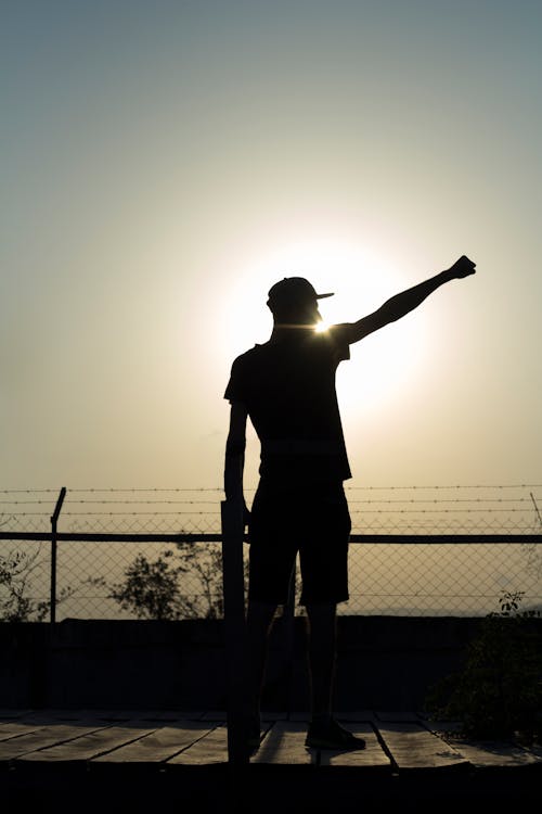 Silhouette of Man Standing Near Fence