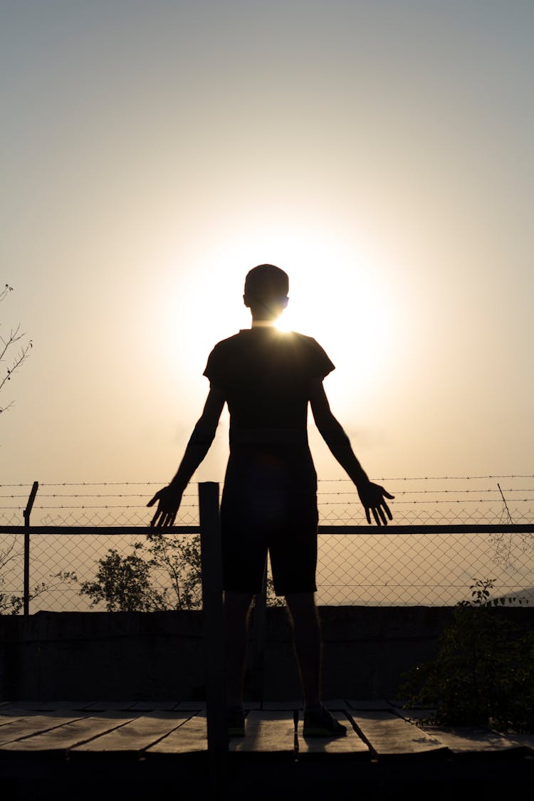 Silhouette Of Man Standing Near Fence