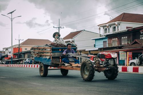 Free Two individuals driving a tractor on a city road, showcasing urban and rural blend. Stock Photo