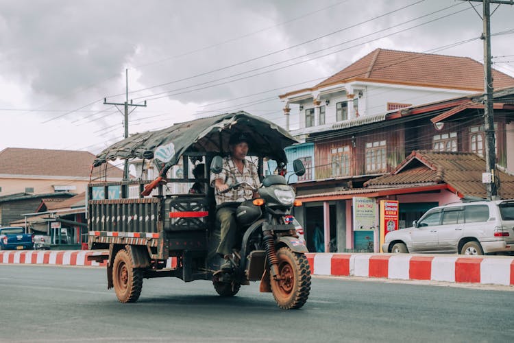 Ethnic Man Driving Old Tuk Tuk On City Road