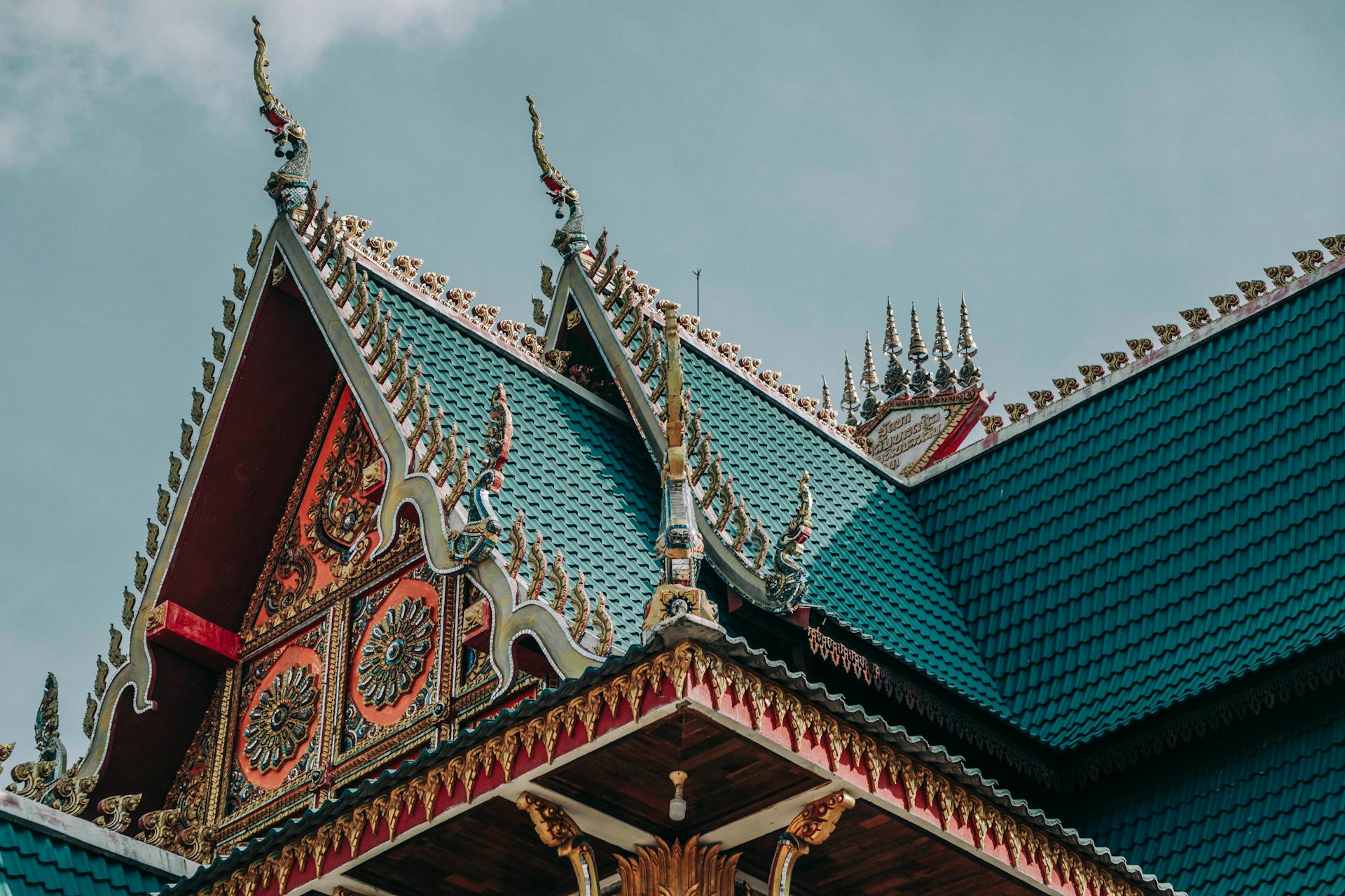 From below of bright ornamental roof with pointed peaks of aged Asian church under cloudy sky