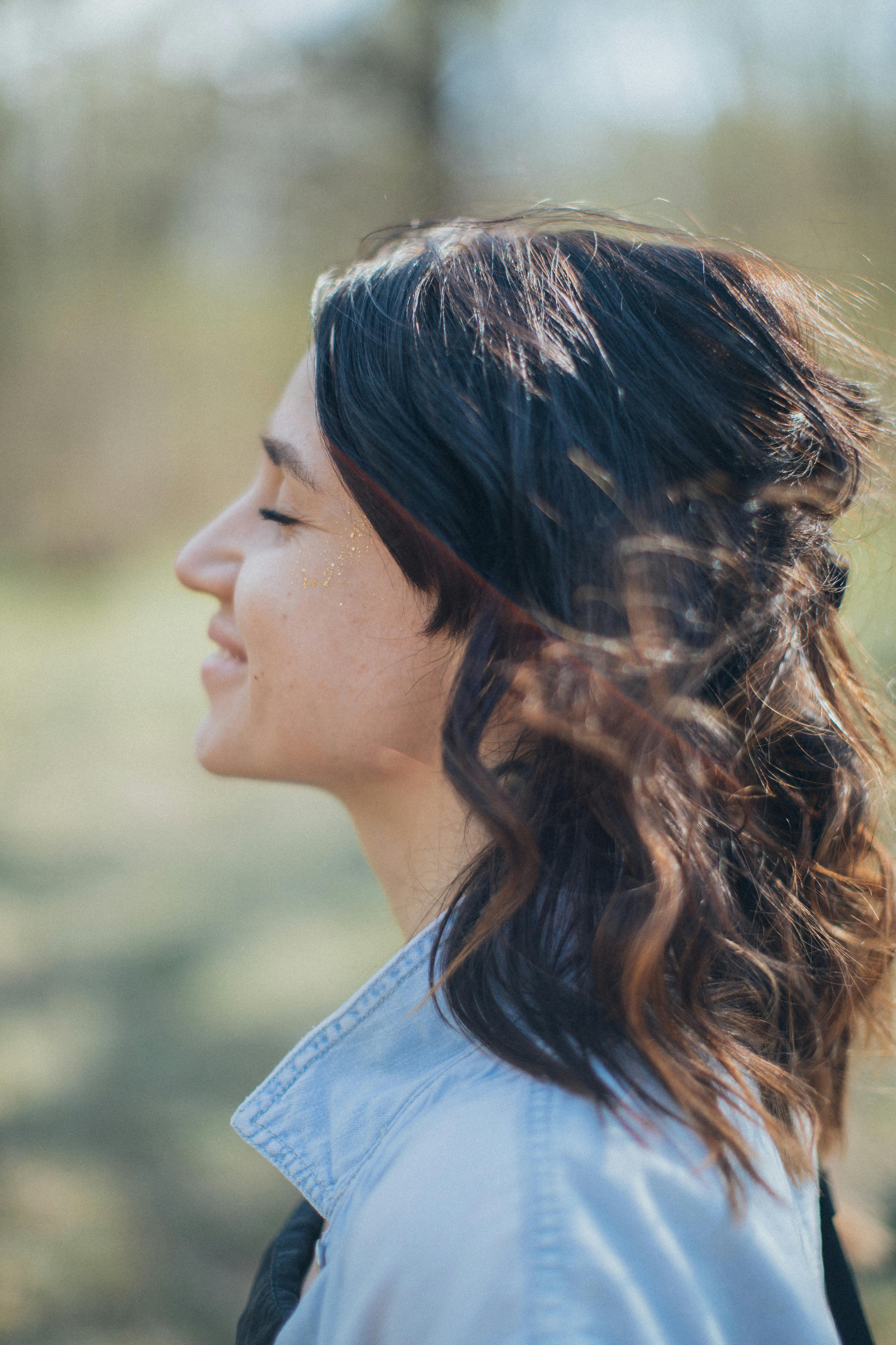 Side profile of a woman smiling outdoors with blurred natural background.