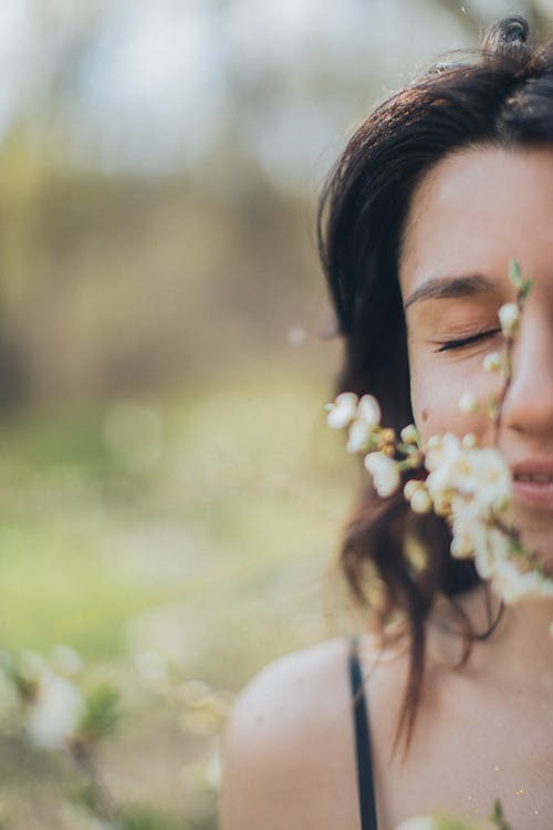 Crop woman smelling blooming flowers in park