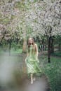 一名赤脚女子身着绿色连衣裙，行走在盛开的樱花下，散发着宁静与自然之美