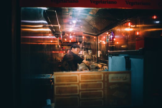 Back view of serious ethnic cook preparing Asian food in kitchen in local cafeteria at night under shining lights and looking away