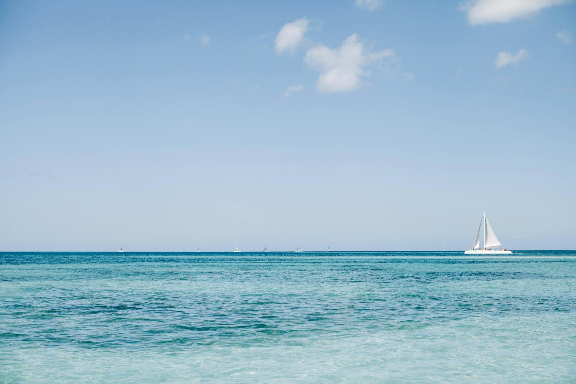 A tranquil ocean view with a sailboat on the horizon under a blue sky.