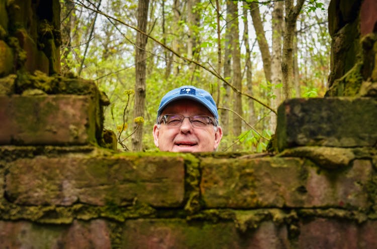 Smiling Mature Man Peeking Out From Behind Old Brick Fence