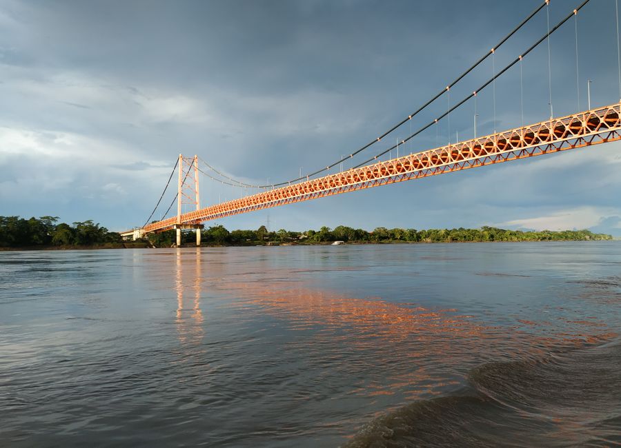 Scenic view of a suspension bridge reflecting in a river at sunset in Puerto Maldonado, Peru.