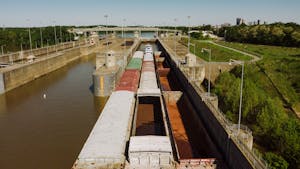 From above of old barge carrying heavy metal containers on canal between growing trees in city port under sky