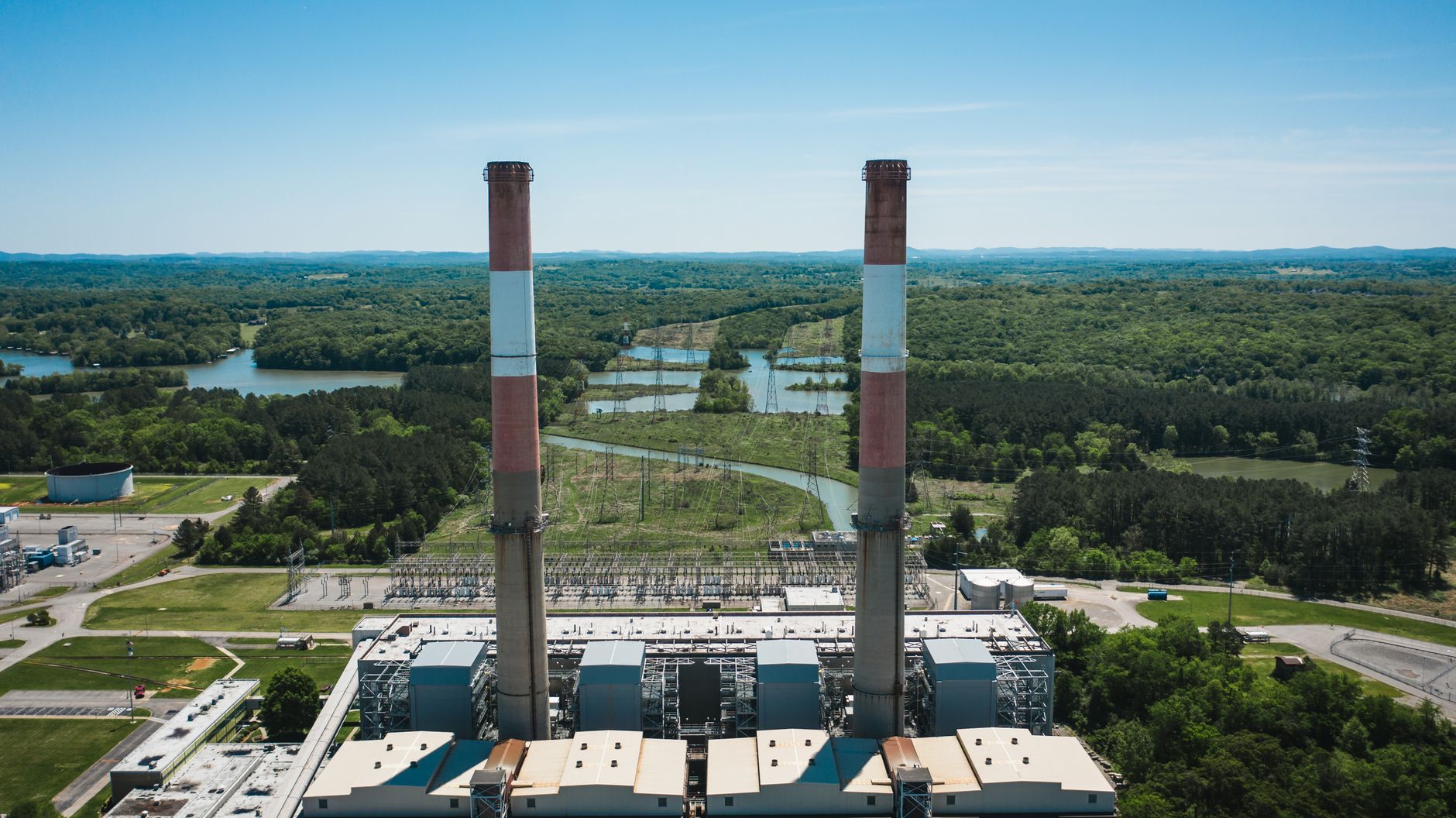 From above of high concrete factory chimneys on generating station platform surrounded by green forest under blue cloudy sky