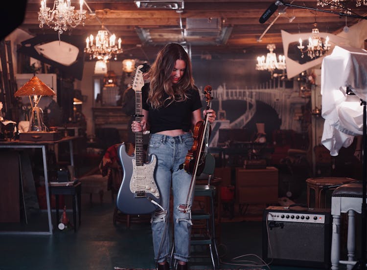 Photo Of Woman Standing While Holding An Electric Guitar And Violin