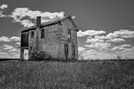 低角度的黑白影像中，旧砖石建筑墙壁风化，草坪上立着烟囱，天空飘着云