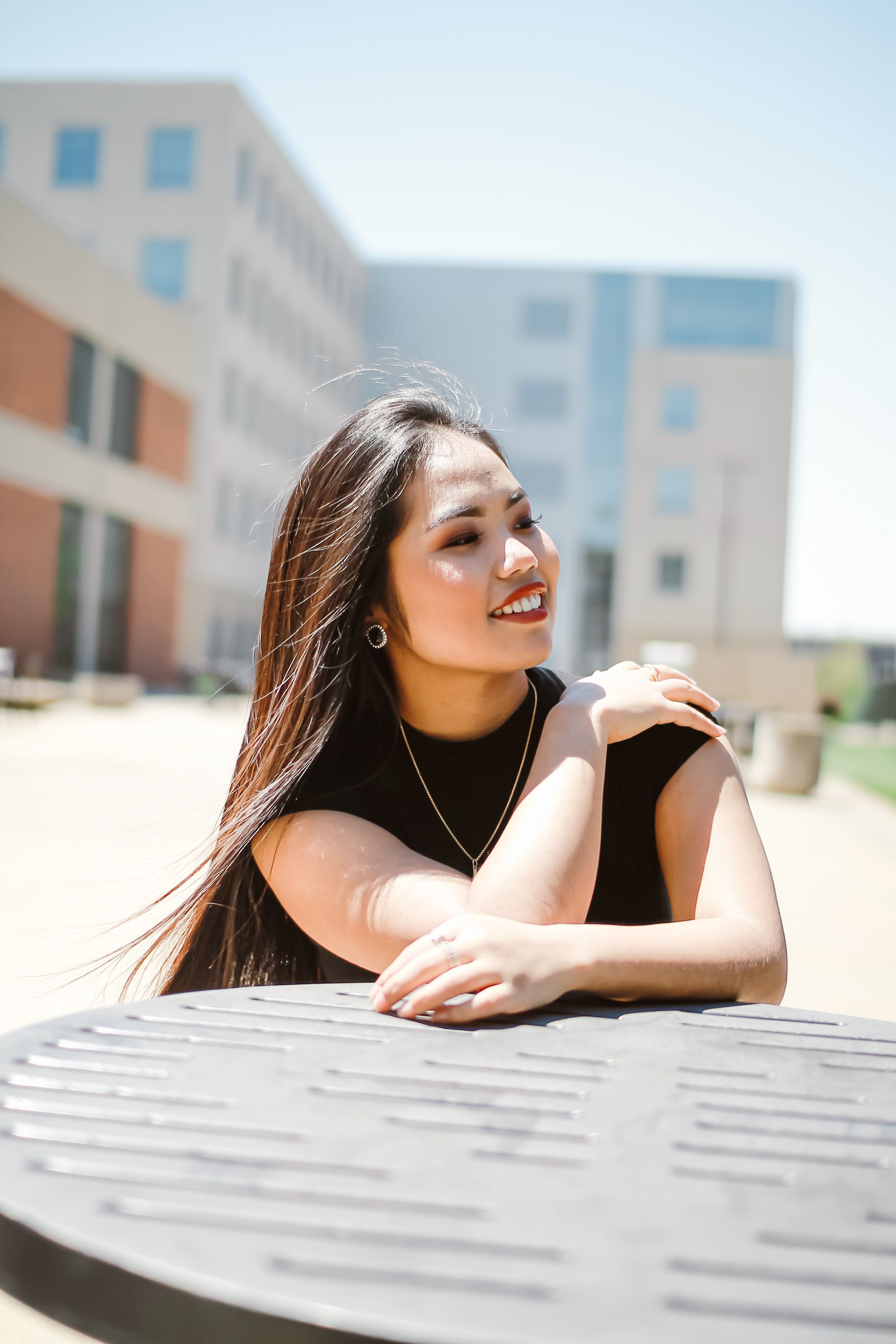 A cheerful woman in a black top smiles outdoors on a sunny day, embodying joy and happiness.