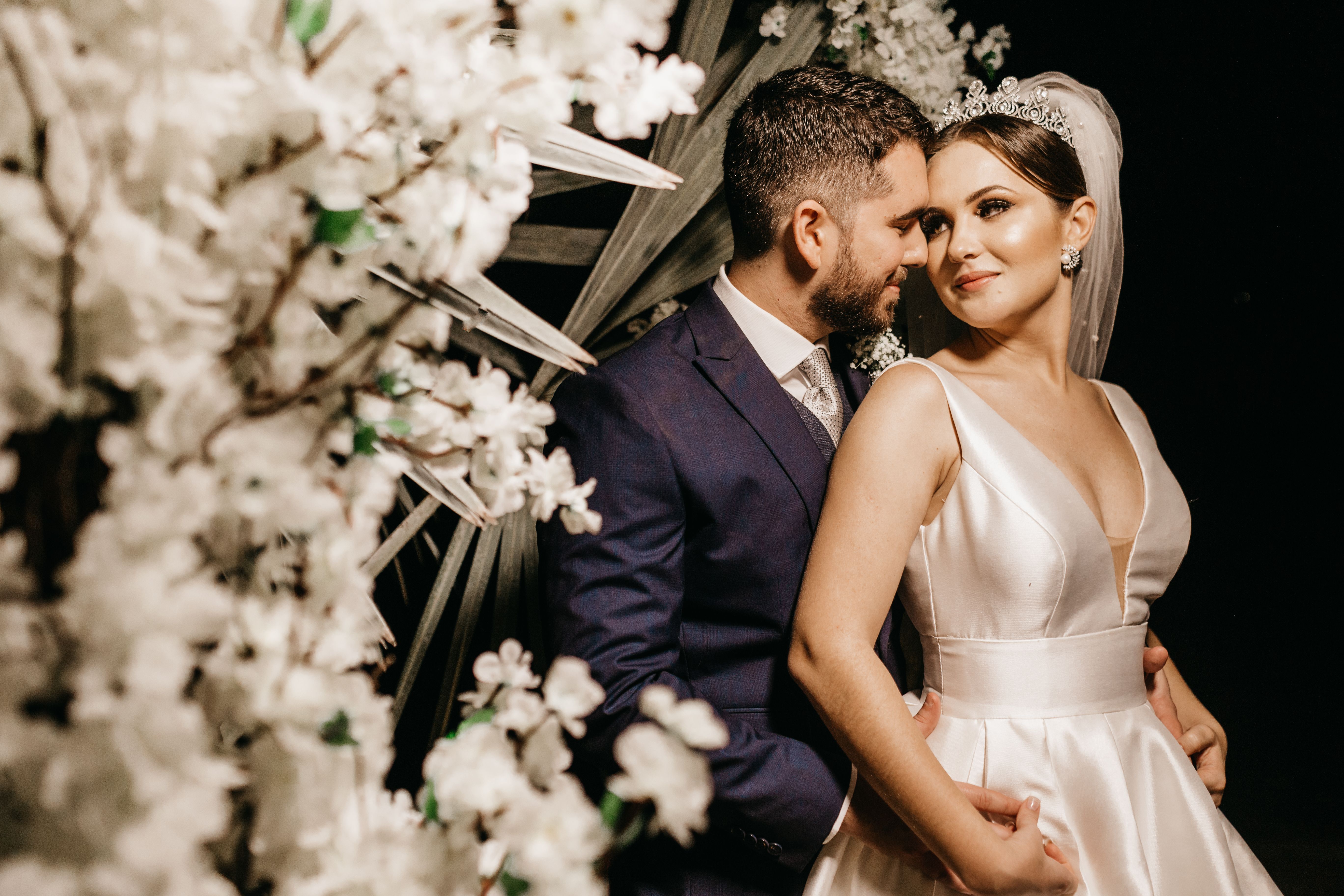 From above side view of content ethnic groom in elegant suit embracing smiling bride in dress near flower decoration during wedding ceremony while looking at each other