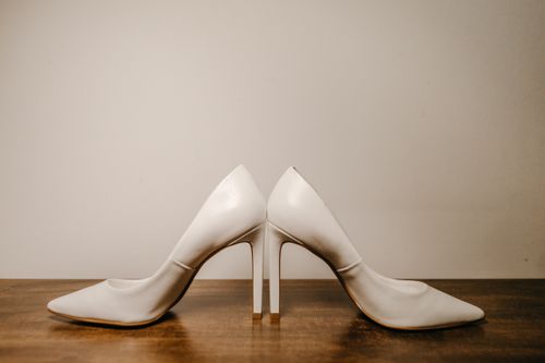 Free Still life of elegant white high heel shoes placed on wooden table near wall Stock Photo