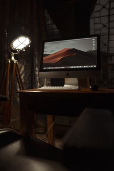Dimly lit workspace with a computer on a wooden desk, ideal for a cozy home office setup.