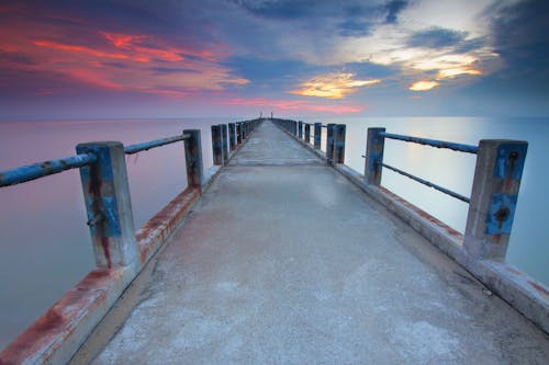 Perspective view of empty pier located over calm sea water under evening sky full of clouds