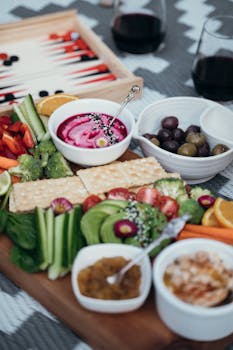 A colorful vegan picnic platter featuring hummus, olives, vegetables, and crackers. Perfect for outdoor gatherings.