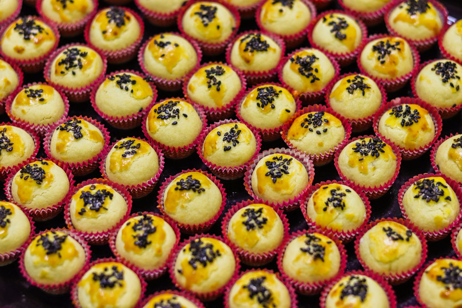 A display of freshly baked mini cupcakes topped with black sesame seeds in vibrant red liners.