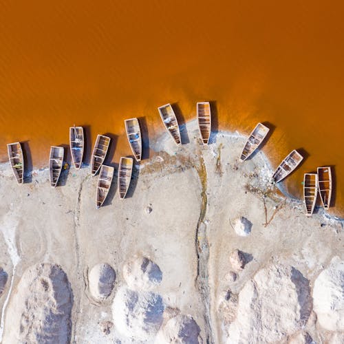 Drone view of small boats moored on white sandy shore of yellow muddy river