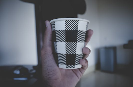 A hand holding a black and white geometric pattern coffee cup indoors.