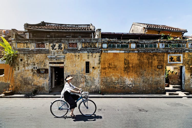 A Woman Riding A Bike In Front Of An Old Building In Vietnam