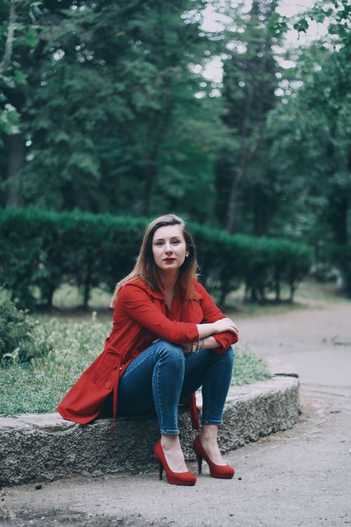 Free Caucasian woman in a red coat and heels sitting outdoors in a park in Georgia. Stock Photo