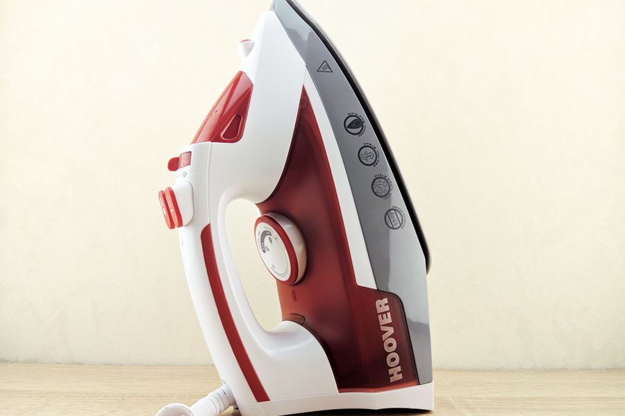 Contemporary multi functional wired iron of white and red colors placed on heel rest on white surface