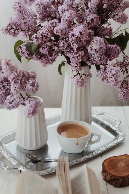 A cozy scene featuring purple lilacs in vases and a cup of coffee on a silver tray.