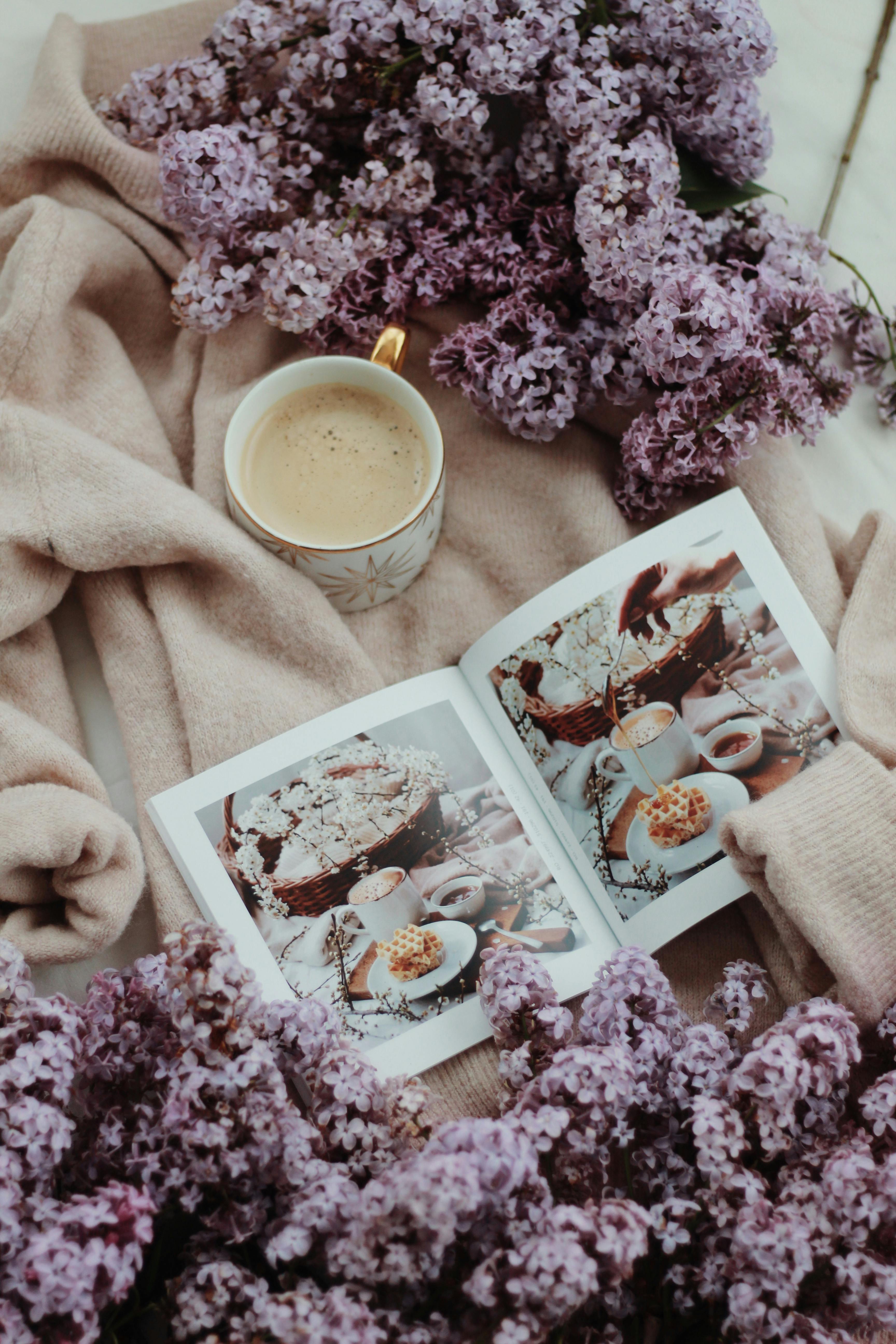 cup of coffee placed on cozy robe near lilac flowers