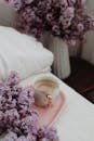 From above elegant cup with cappuccino served on tray on comfy bed and decorated with lush lilac bouquet in cozy bedroom