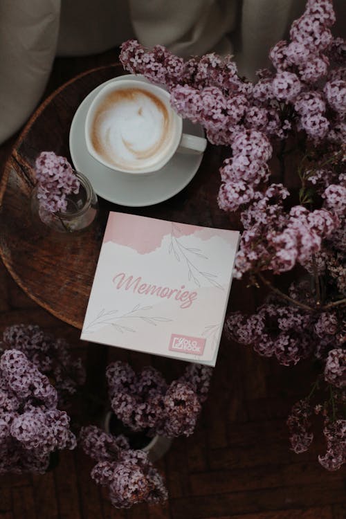 Free From above composition of delicious fresh cappuccino served on round bedside table with postcard decorated with delicate lilac bouquet on spring morning Stock Photo