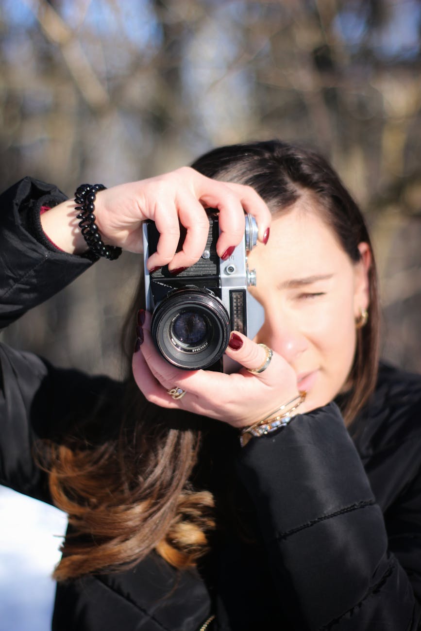 A woman in a black jacket focuses keenly while taking a photograph outdoors.