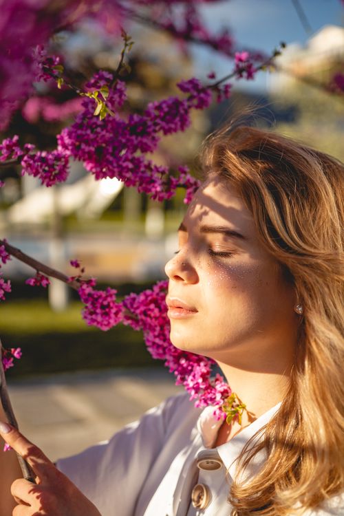 Free A peaceful woman enjoying spring blooms in sunlight with eyes closed, showcasing serenity and beauty. Stock Photo