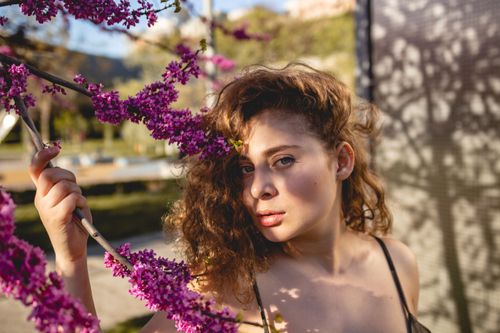 Free Young woman with curly hair and pink flowers enjoying a sunny spring day outdoors. Stock Photo